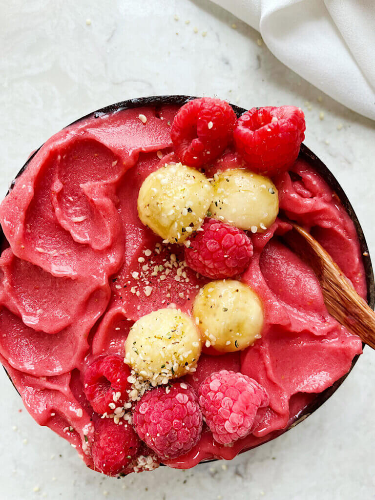 thick strawberry smoothie bowl in a coconut bowl topped with raspberries banana and hemp seeds