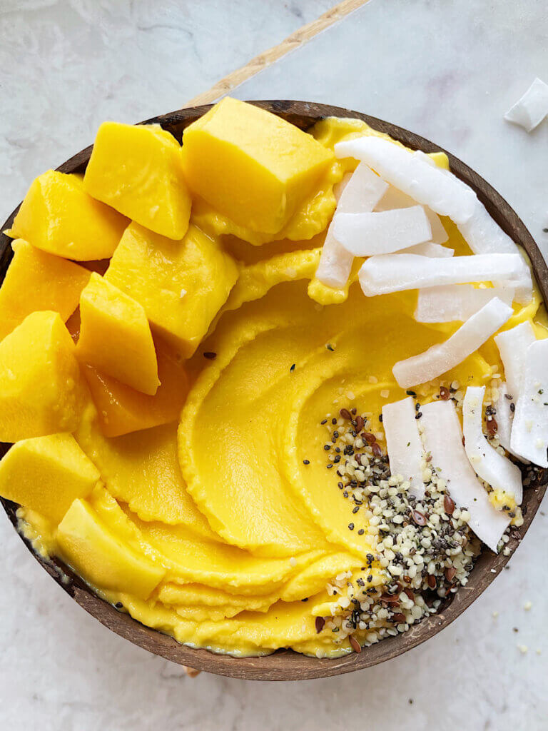 thick mango smoothie bowl with no banana in a coconut shell bowl