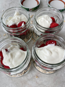 raspberries and vanilla yogurt on top of oats and chia seeds in glass jars