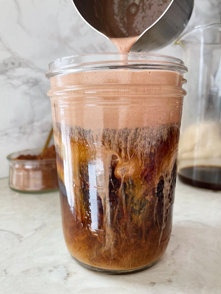 pouring chocolate cold foam at home over iced coffee