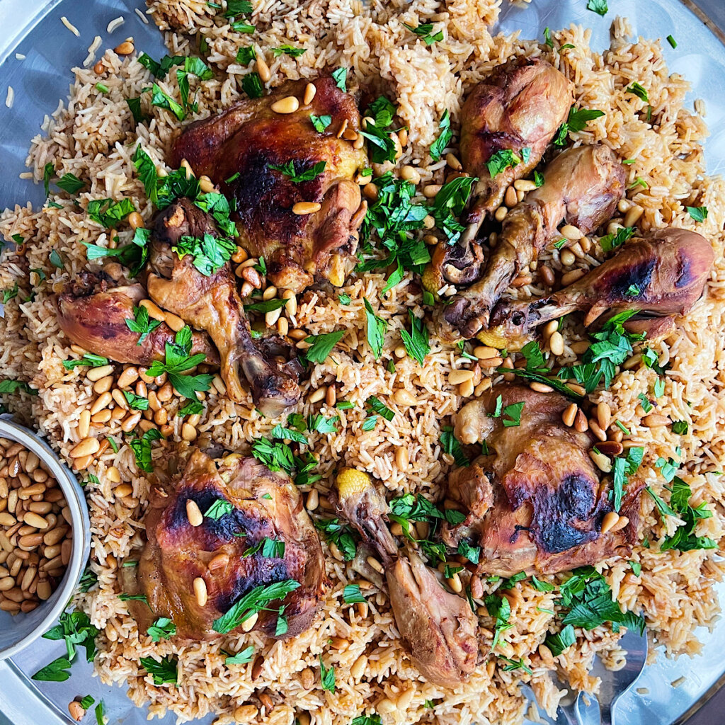 Chicken kabsa recipe on a serving platter with pine nuts and parsley